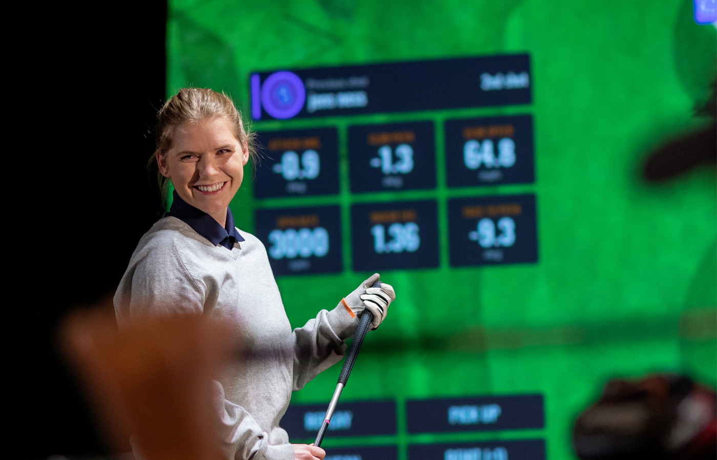 Smiling lady holding golf club in front of golf screen
